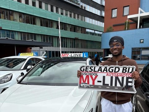 Geslaagde leerling met het bord Geslaagd bij MY-Line voor de witte lesauto