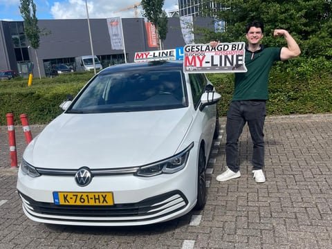 Geslaagde leerling met het bord Geslaagd bij MY-Line naast de witte lesauto