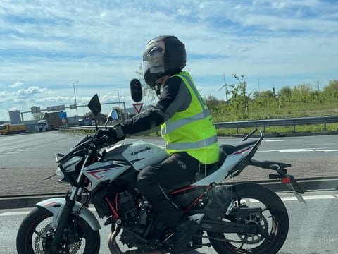 Motorleerling met helm en geel hesje op de witte lesmotor in het verkeer