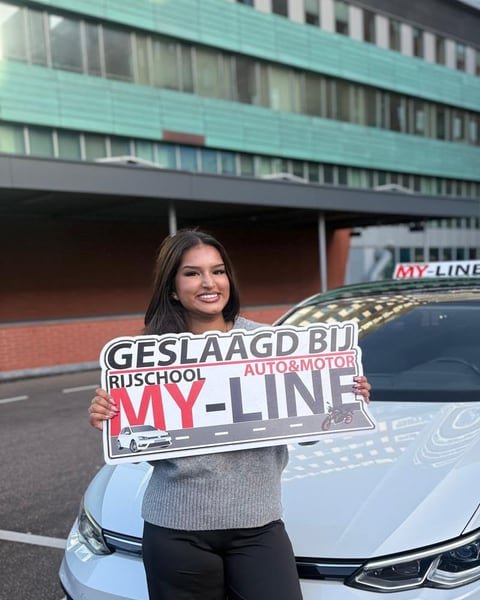 Geslaagde leerling met het bord Geslaagd bij MY-Line voor de witte lesauto