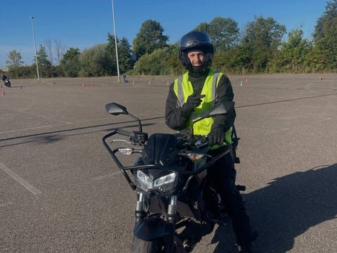 Motorleerling met helm en geel hesje op de lesmotor op een groot terrein