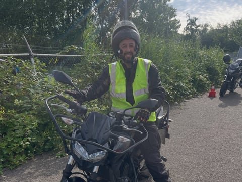 Motorleerling met helm en geel hesje op de lesmotor op een pad