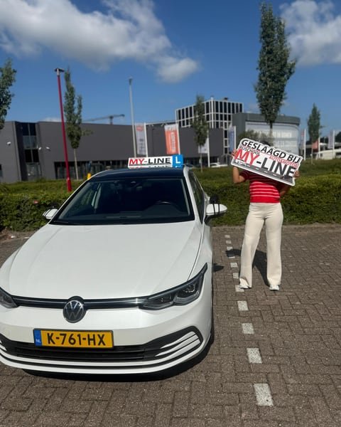 De witte Volkswagen Golf van MY-Line met het dakbord, een geslaagde houdt het bord omhoog