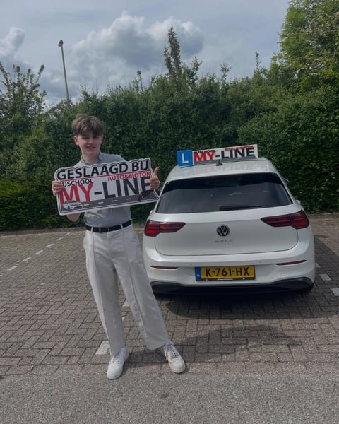 Geslaagde leerling met het bord Geslaagd bij MY-Line naast de achterkant van de lesauto