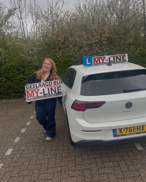 Geslaagde leerling met het bord Geslaagd bij MY-Line naast de achterkant van de lesauto