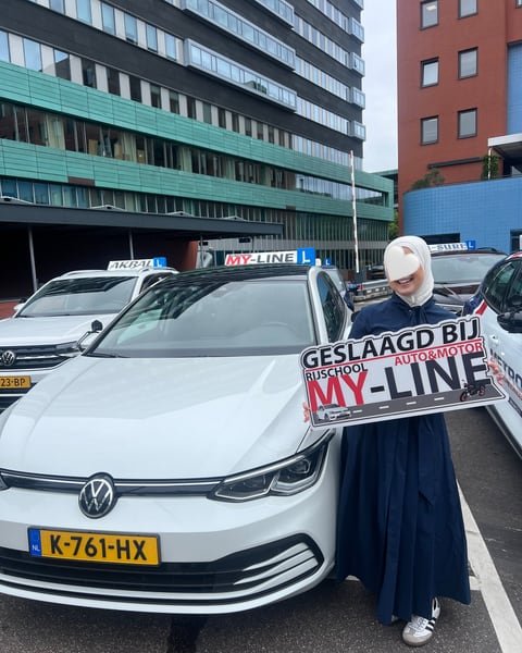 Geslaagde leerling met het bord Geslaagd bij MY-Line bij de witte lesauto