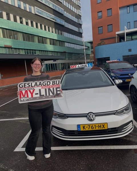 Geslaagde leerling met het bord Geslaagd bij MY-Line bij de witte lesauto