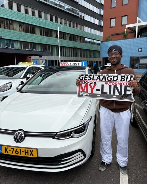 Geslaagde leerling met het bord Geslaagd bij MY-Line bij de witte lesauto