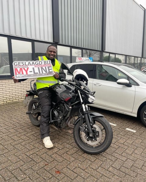 Geslaagde motorrijder op de lesmotor houdt het bord Geslaagd bij MY-Line omhoog