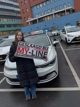 Geslaagde leerling met het bord van MY-Line bij de lesauto of lesmotor