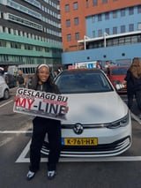 Geslaagde leerling met het bord van MY-Line bij de lesauto of lesmotor